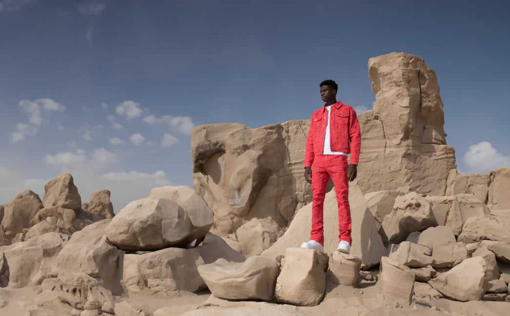 Person in a red Guapi Jeans outfit standing on rocky desert terrain with a clear blue sky.